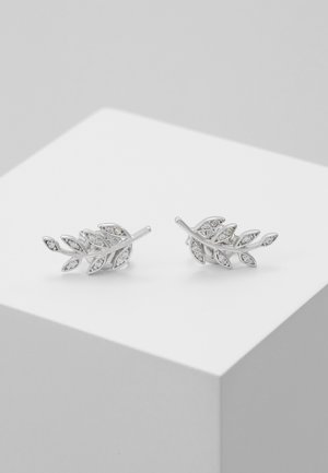 Paire de boucles d'oreilles clous en forme de feuille en argent avec petits cristaux incrustés, présentée sur un socle cubique blanc.