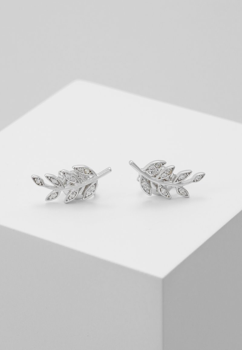 Paire de boucles d'oreilles clous en forme de feuille en argent avec petits cristaux incrustés, présentée sur un socle cubique blanc.