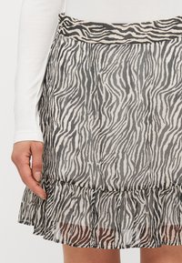 Svart og hvit zebra-mønstret skjørt med volangkant, laget av et lett og transparent stoff. Har en tettsittende midje.