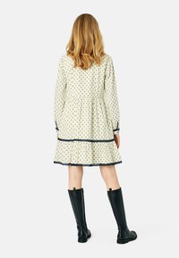 Langärmliges cremefarbenes Kleid mit marineblauem Sternenmuster, gestuftem Rock und Augenlet-Spitzenbesatz, kombiniert mit knielangen schwarzen Lederstiefeln.