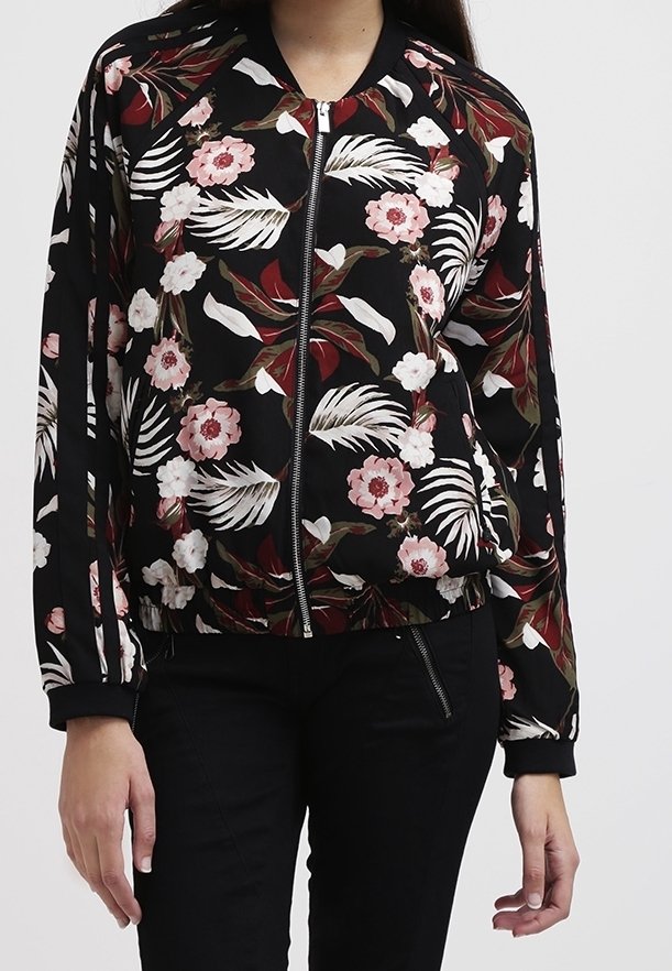 Sort lynlåsjacket med pink og hvide blomster- og bladmønstre, båret med sorte bukser.