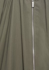 Gros plan d'un tissu kaki avec une fermeture éclair métallique verticale argentée au centre.