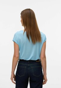 Top azzurro chiaro a maniche corte con vestibilità rilassata, texture liscia e orli arrotolati, abbinato a jeans in denim scuro con tasche posteriori.