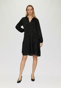 Robe noire à volants avec des manches longues et un décolleté en V. Fabriquée en tissu léger avec des rayures verticales. Silhouette élégante et fluide.