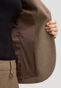 Blazer marrone a motivo houndstooth con una morbida fodera in satin marrone. Top nero a coste sotto, che mette in mostra un design aderente e un tessuto testurizzato.