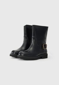 Black leather ankle boots with a smooth finish, rounded toes, and a decorative gold-tone buckle on the side. Flat rubber soles.