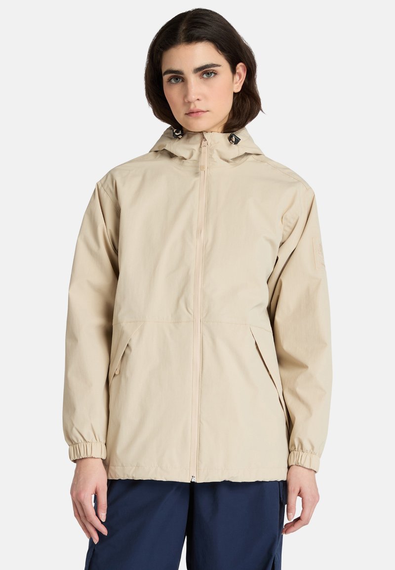 Beige lättviktsjacka med huva, elastiska ärmslut, framdragkedja och sidofickor, tillverkad av slät, vattenavvisande tyg.