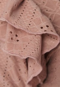 Pehly pink színű kötött anyag, díszítő mintával, kis lyukakkal és fodros szélekkel. Simább felületű, textúrált.