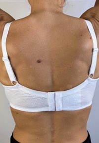 Sujetador deportivo blanco con tejido texturizado, tirantes ajustables y un cierre de gancho y ojo en la parte posterior. Material suave y diseño sencillo.