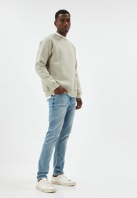 Felpa grigia chiara con polsini e orlo a costine, abbinata a jeans azzurri e sneakers bianche. Un look semplice, casual e confortevole.