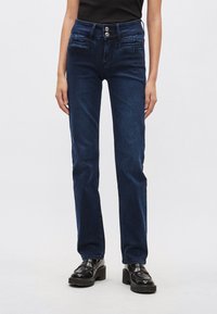 Sötétkék egyenes szabású farmernadrág, magas derékkal és két első zsebbel. A derékrésznél két fém gomb található.