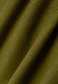Tessuto in verde oliva con una superficie morbida e testurizzata. Il tessuto si drappeggia delicatamente, mettendo in mostra schemi di tessitura raffinati e sottili variazioni di colore.