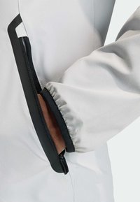 Witte jas met een getailleerd ontwerp. Voorzien van een zwarte rits en elastische boorden. Glad oppervlak met een contrasterende bies langs de opening.