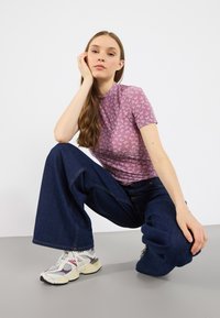 Hellblaues kurzärmeliges Oberteil mit einem strukturierten Schmetterlingsmuster, kombiniert mit weit geschnittenen dunkelblauen Jeans und klobigen weißen Sneakern.