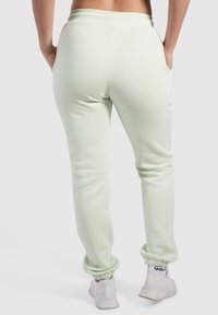 Ljusgröna joggers i mjukt tyg, med elastisk midja, sidofickor och smalnande ärmslut. Bärs med vita träningsskor.