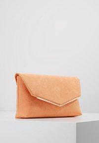 Brožurka z broskvového semiše se trojúhelníkovým klopovým uzavřením a stříbrnými detaily. Měkká textura, obdélníkový tvar a minimalistický design.