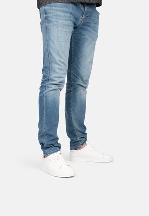 Jeans in denim azzurro chiaro con vestibilità slim e finitura sbiadita, abbinati a sneakers bianche con texture liscia e design minimale.