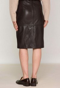 Jupe crayon en cuir marron avec des coutures et une fermeture éclair au dos. Associée à des mocassins marron foncé, mettant en avant un design ajusté et une texture lisse.