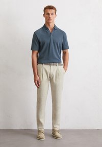 Polo shirt azzurro chiaro a maniche corte con un motivo testurizzato, abbinato a pantaloni in lino beige. L'outfit include una cintura intrecciata e scarpe beige.