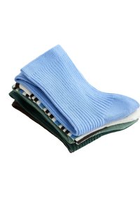 Pile de chaussettes côtelées pliées en bleu, blanc, vert et à motifs rayés sur fond blanc.