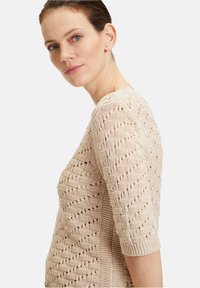 Beige gestrickter Pullover mit einem strukturierten Muster, kurzen Ärmeln und einem runden Halsausschnitt, der das offene Gewebe und das atmungsaktive Design hervorhebt.