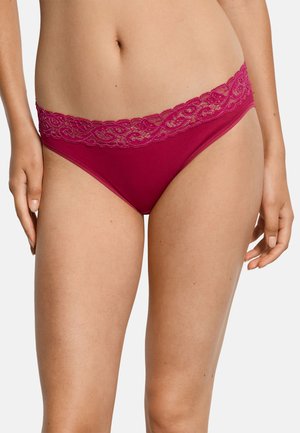 Kobieta w ciemnoróżowym bikini z koronkową lamówką, pokazana od talii do połowy uda, z rękami swobodnie opuszczonymi wzdłuż ciała.