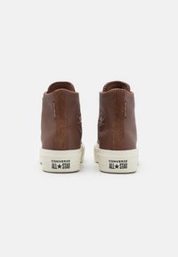 Brązowe skórzane sneakersy typu high-top z teksturowanym wykończeniem, białą gumową podeszwą i wytłoczonym logo gwiazdy z tyłu.