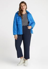 Chaqueta acolchada azul con capucha, con una parte superior acolchada. Combinada con una camisa de rayas azul marino y pantalones cortos azul marino, complementada con zapatillas blancas.