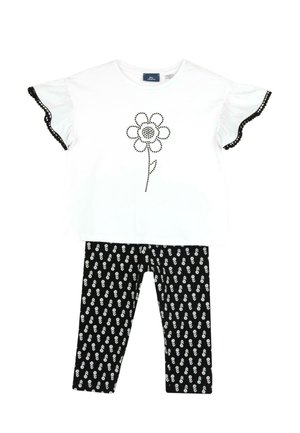 Top bianco a maniche corte con bordi neri e design floreale, abbinato a leggins neri con un motivo floreale bianco.