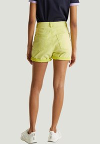 Limoengroene denim shorts met omslagen, vijf zakken en een hoog tailleontwerp, gecombineerd met witte sportschoenen.