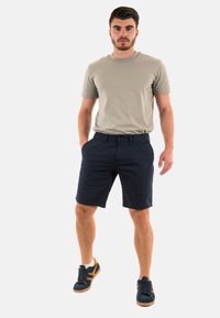 T-shirt en coton beige, shorts bleu marine et baskets foncées avec des accents clairs. Le T-shirt a des manches courtes, les shorts ont des poches et une fermeture à bouton.