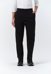 Zwarte, lichte elastische broek met zijzakken, taps toelopende pijpen en een gladde textuur, gedragen met zwarte wandelschoenen.