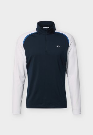 Herre sportstrøje med lange ærmer, navyblå overdel, hvide ærmer, kvart-lynslåslukning ved halsen og lille hvidt logo på venstre bryst.