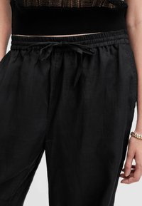 Zwarte linnen broek met een elastische tailleband, strikdetail aan de voorkant en een relaxte pasvorm. Zachte textuur, geen zichtbare patronen of hardware.