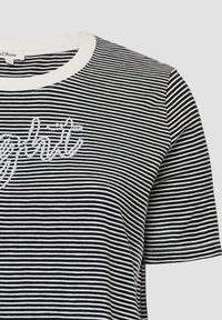 Zwart-witte gestreepte t-shirt met een ronde hals, voorzien van getextureerde witte geborduurde accenten in cursieve stijl.
