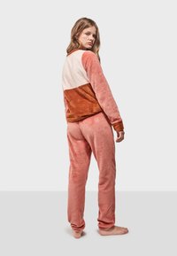 Fleece-Loungewear-Set mit einem farblich abgestimmten Sweatshirt in Hellrosa, Orange und Braun, dazu passende rosa Hosen. Weicher Stoff, entspannter Schnitt.