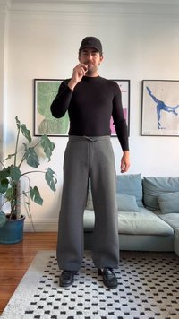 Cămașă neagră cu mâneci lungi, potrivită, pantaloni de trening gri cu croială largă și pantofi negri. Decorul include o planta și lucrări de artă pe perete.