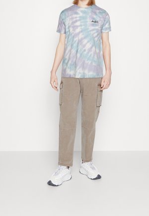 Lys lilla og blå tie-dye t-shirt med korte ærmer og et lille logo på brystet, parret med khaki cargo bukser med sidelommer og hvide sneakers.