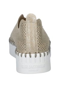 Zapato sin cordones color beige claro con parte superior texturizada, acentos metálicos, suela de goma blanca y costuras contrastantes a lo largo del borde.