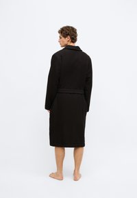 Melns vafelēs teksturēts halāts ar šaļu apkakli, garām piedurknēm un jostu viduklī, garums līdz pusstilbam, ar gludu auduma apdari.