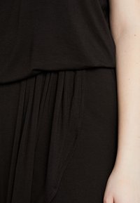 Svart klänning med mjukt, lätt tyg och en flödande design. Den har veck vid midjan som skapar en avslappnad passform och drapering.