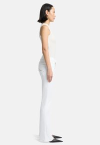 Weißes ärmelloses Oberteil kombiniert mit weißen ausgestellten Jeans; Schuhe mit spitzem Zehen; glatter Stoff und minimalistisches Design, von der Seite präsentiert.