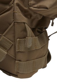 Coin d'un sac à dos en tissu marron montrant des sangles tissées, une fermeture à cordon en plastique et des détails de couture durables.