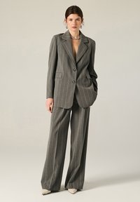 Completo grigio a righe con giacca doppiopetto e lembi larghi, pantaloni a vita alta e dal taglio morbido. Tessuto liscio e strutturato.