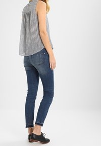 Top senza maniche a motifs con retro plissettato; jeans skinny blu scuro con orlo grezzo; scarpe nere con lacci.