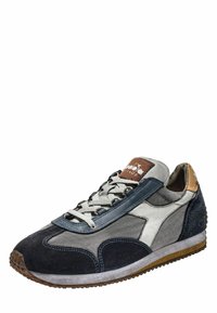 Scarpa sportiva in grigio, blu navy e bianco in suede con una texture a motivi. Presenta una suola piatta e una chiusura con lacci nella parte anteriore con un accento marrone chiaro a contrasto.