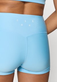 Κοντινό πλάνο ενός ατόμου που φοράει ανοιχτό μπλε αθλητικά σορτς ψηλής μέσης με μικρά λευκά γράμματα στη μέση, εμφανίζοντας την κάτω πλάτη και τους γοφούς.