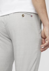 Light grey pants made from textured fabric, featuring a side pocket with a button closure and small striped accent on the pocket.