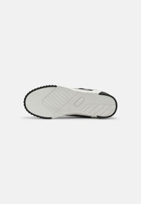 Black and white sneaker sole features textured rubber for traction, with a patterned midsole and distinct lateral grooves for flexibility.