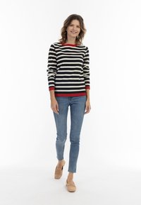 Schwarz- und cremegestreifter Pullover mit rotem Ausschnitt und Saum, kombiniert mit blauen Skinny-Jeans und beigen Slippern.